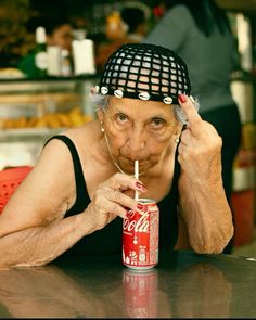 an older woman with a hat on top of her head holding a drink in front of her face