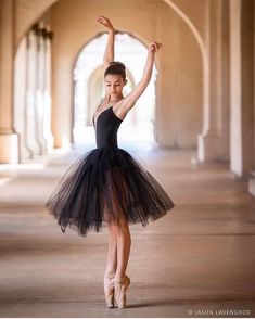 a young ballerina wearing a black tulle skirt and ballet shoes, standing in an archway