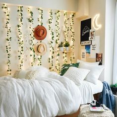 a bedroom with white bedding and green plants on the headboard, along with hanging lights