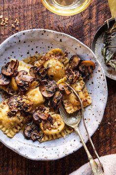 a white plate topped with ravioli and mushrooms next to a glass of wine on top of a wooden table