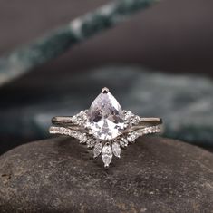 a pear shaped diamond engagement ring on top of a rock with diamonds in the band