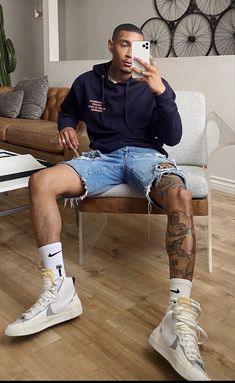 a man sitting on a couch taking a selfie with his cell phone while wearing ripped shorts