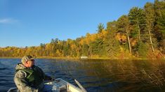 a man on a boat in the middle of a lake surrounded by trees with fall colors