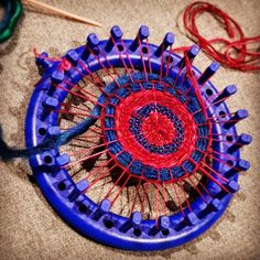 a blue and red object sitting on top of a floor next to some knitting needles