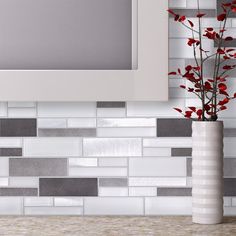 a white vase with red flowers in it next to a wall mounted mirror and tiled backsplash