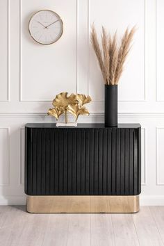 a black cabinet with gold accents and a clock on the wall behind it in a white room