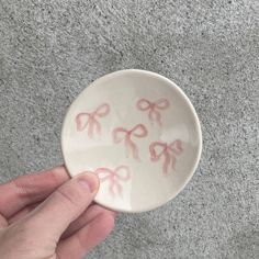 a hand holding a white bowl with pink bows on the inside and bottom, in front of a gray background