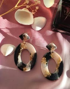 two pairs of earrings sitting on top of a pink cloth next to seashells