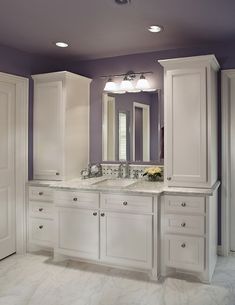 a large bathroom with two sinks and white cabinets in the corner, along with purple walls