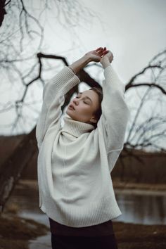 a woman in a white sweater and black skirt holding her arms up above her head