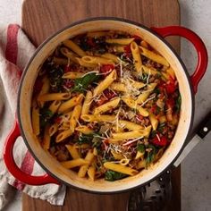 a pot filled with pasta and spinach on top of a wooden cutting board