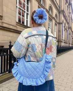 a woman walking down the street carrying a blue and white quilted purse on her back