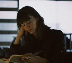 a woman sitting at a desk writing on a book and holding a pen in her hand