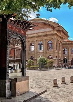 an old building in the middle of a plaza with people walking around and sitting on benches