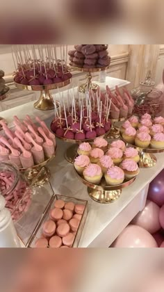 a table topped with lots of cupcakes and desserts covered in pink frosting