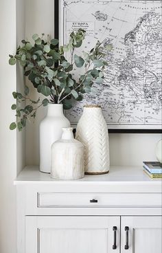 two vases and a plant sit on a white dresser in front of a map