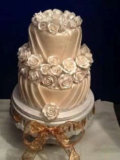 a three tiered wedding cake with white roses on top and gold ribbon around the bottom