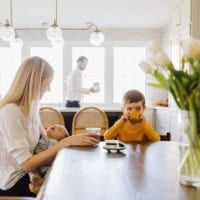 a woman sitting at a table with a child on her lap and another man standing in the background