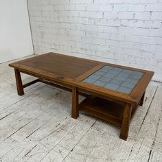 a wooden table with glass top sitting in front of a white brick wall and floor