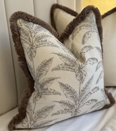 two decorative pillows on a bed with white linens and brown trim around the edges