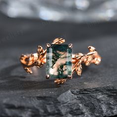 a green ring with leaves on it sitting on top of a black stone slab in front of a rock