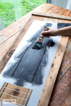 a person is using a brush to paint a piece of artwork on a wooden table