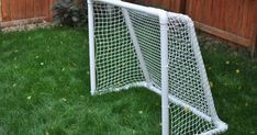 a white soccer goal sitting on top of a green grass covered field next to a wooden fence