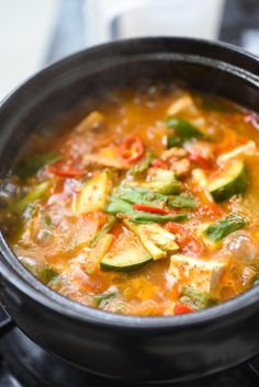 a pot filled with soup and vegetables sitting on top of a stove burner,