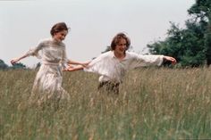 two people are running through tall grass in the field, one is holding his arms out