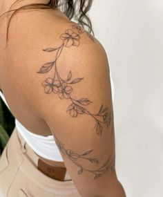 the back of a woman's shoulder with flowers on it and leaves around her arm