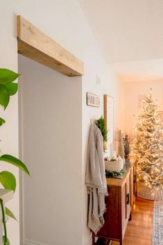 a white christmas tree in the corner of a living room next to a wooden shelf