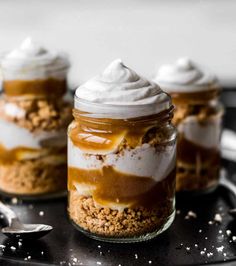 three desserts in glass jars with whipped cream and caramel on top, sitting on a table