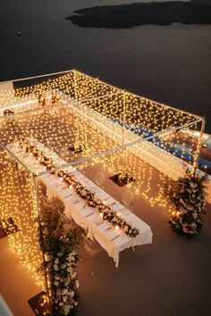 an aerial view of a table set up with lights and flowers on the tables in front of water