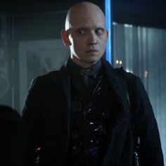 a bald man in a black jacket and tie looking at the camera with an evil look on his face