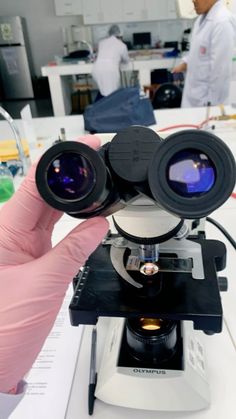 a person holding up a microscope with two lenses on it's top and another in the background