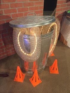 a bucket with some lights in it on the floor next to orange cones and a brick wall