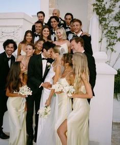 a group of people standing next to each other in front of a white wall with flowers