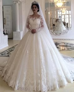 a woman wearing a wedding dress with long sleeves and lace on the skirt is standing in front of a mirror