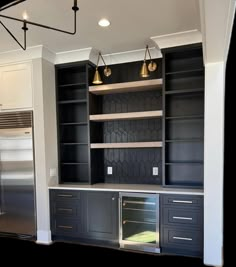 an empty kitchen with black cabinets and silver appliances in the center, along with gold pendant lights hanging from the ceiling