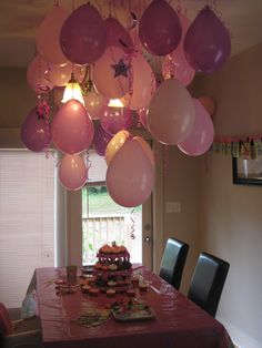 a party table with pink and white balloons hanging from the ceiling