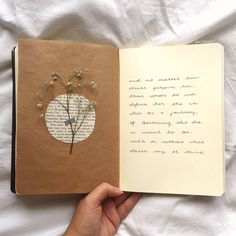 a hand holding an open book with writing on it and flowers in the pages,