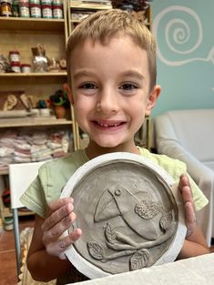 a young boy holding up a clay plate with an elephant on it's face