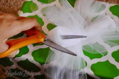 someone cutting fabric with scissors on top of a green and white flowered table cloth