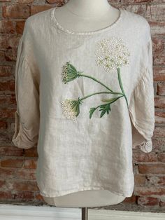 a white top with flowers on it sitting next to a brick wall