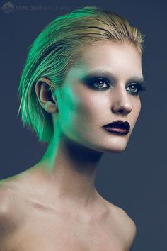 a woman with bright green hair and black makeup is posing for a photo in front of a gray background