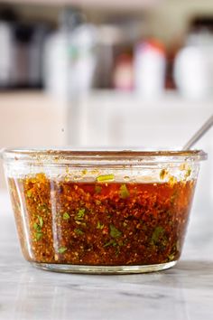 a glass jar filled with red sauce and herbs