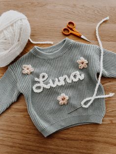 a knitted sweater with the word guru written on it next to yarn and scissors