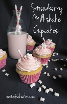 three cupcakes with pink frosting and marshmallows next to a bottle of milk