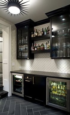 a home bar with black cabinets and marble flooring, lighted by a chandelier