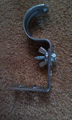 a metal hook with two screws attached to it on the floor next to a carpet